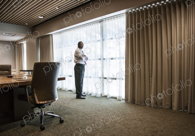 Black businessman standing at a window next to a large conference table.
