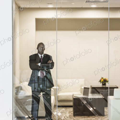 Black businessman standing in conference room window. Black businessman standing in conference room window.