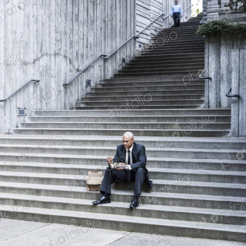 Black businessman taking a break for lunch sitting on a stairway step. Black businessman taking a break for lunch sitting on a stairway step.