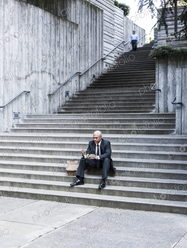 Black businessman taking a break for lunch sitting on a stairway step.