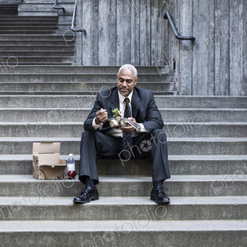 Black businessman taking a break for lunch sitting on a stairway step.