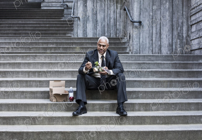 Black businessman taking a break for lunch sitting on a stairway step.