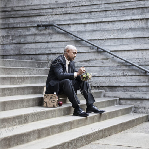 Black businessman taking a break for lunch sitting on a stairway step. Black businessman taking a break for lunch sitting on a stairway step.