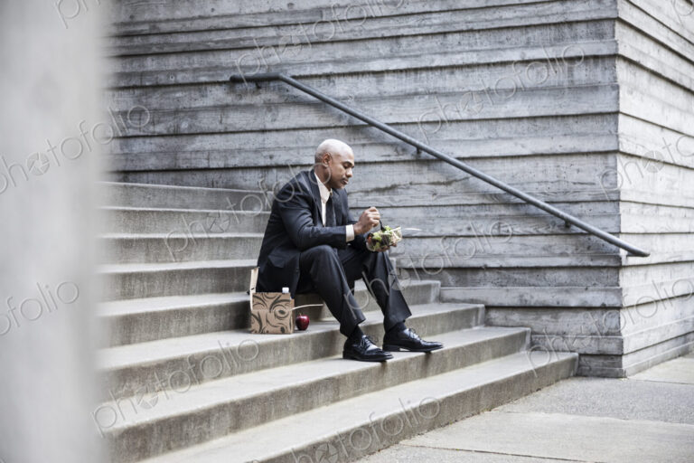 Black businessman taking a break for lunch sitting on a stairway step.