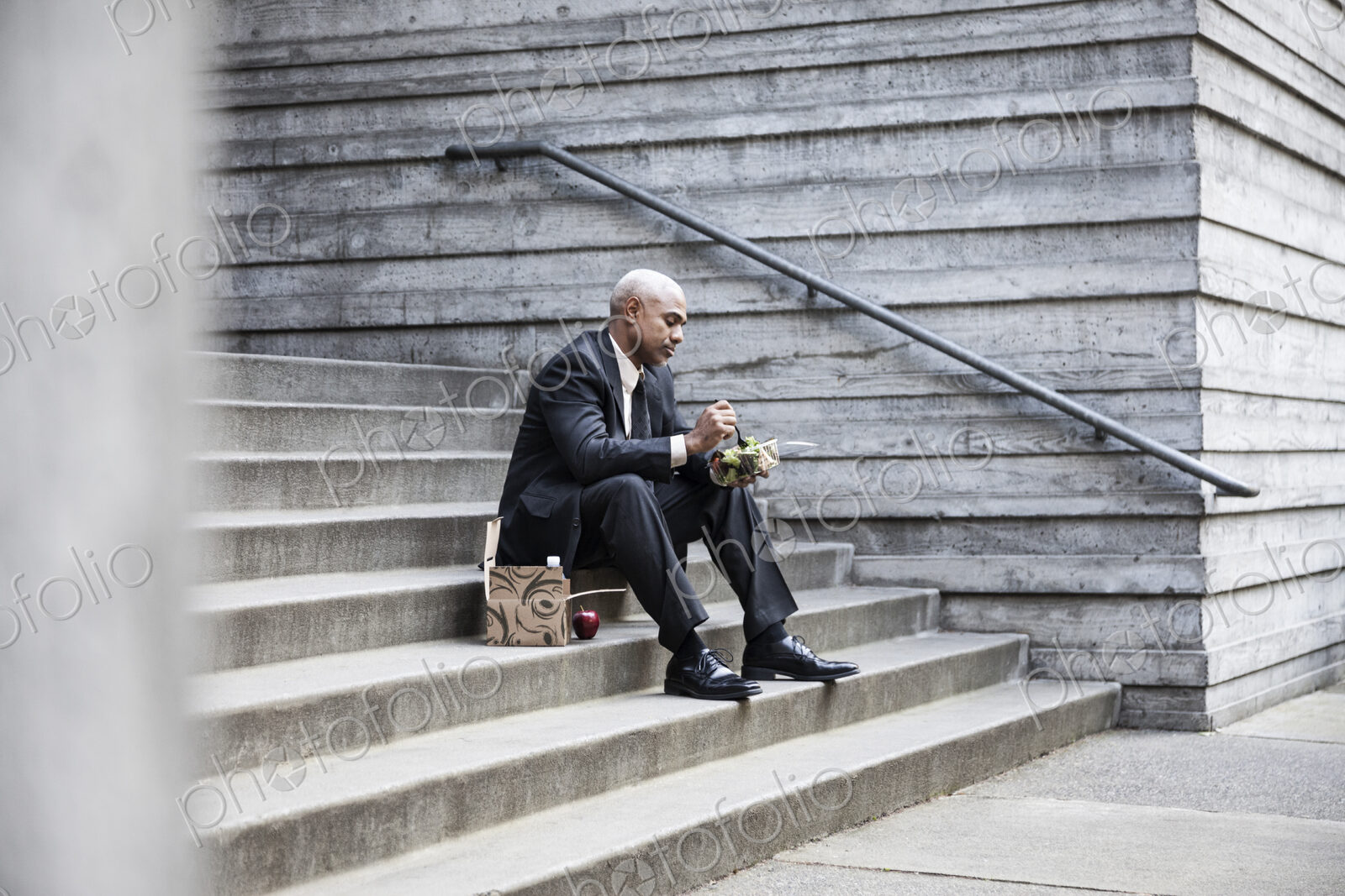 Black businessman taking a break for lunch sitting on a stairway step.