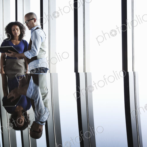 Black businesswoman and Asian businessman looking at a notebook computer and reflected…