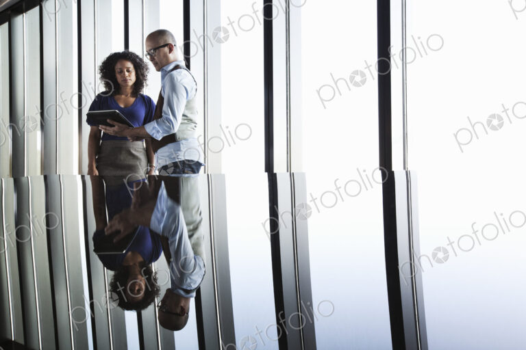 Black businesswoman and Asian businessman looking at a notebook computer and reflected…