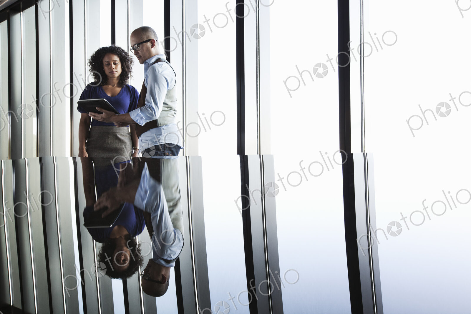 Black businesswoman and Asian businessman looking at a notebook computer and reflected…