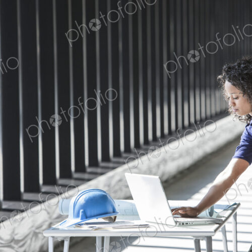 Black businesswoman working on a computer at a desk in a large empty office space.