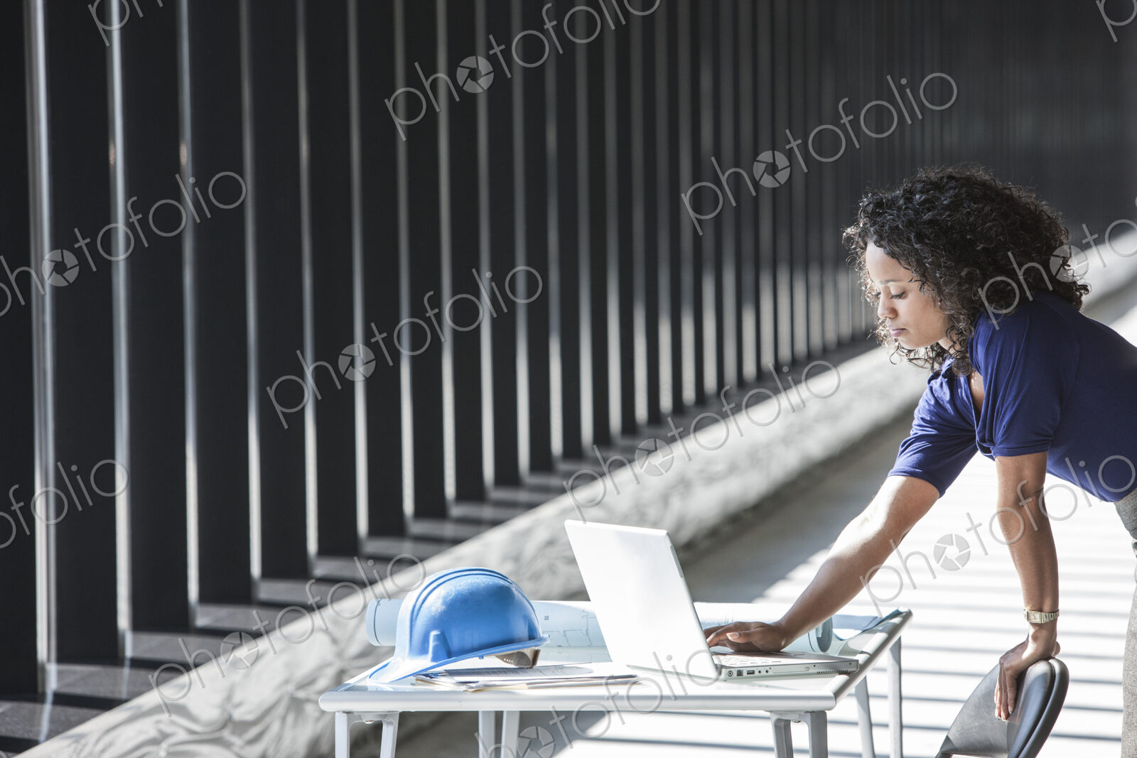 Black businesswoman working on a computer at a desk in a large empty office space.