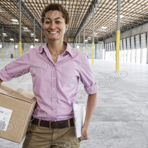 Black female holding cardboard box and standing in front of loading dock doors in a… Black female holding cardboard box and standing in front of loading dock doors in a…