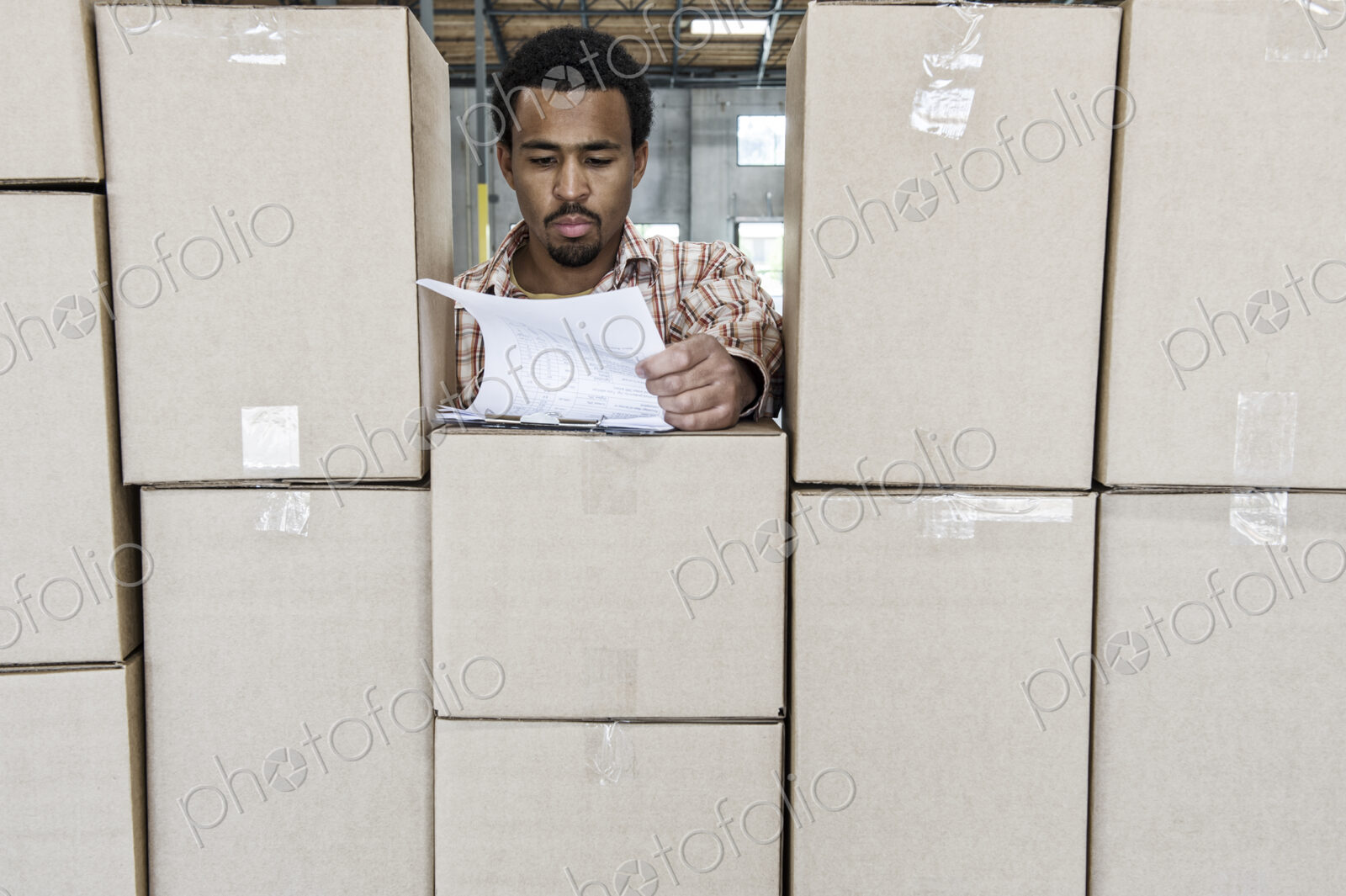 Black male worker checks inventory of new boxes in a warehouse.