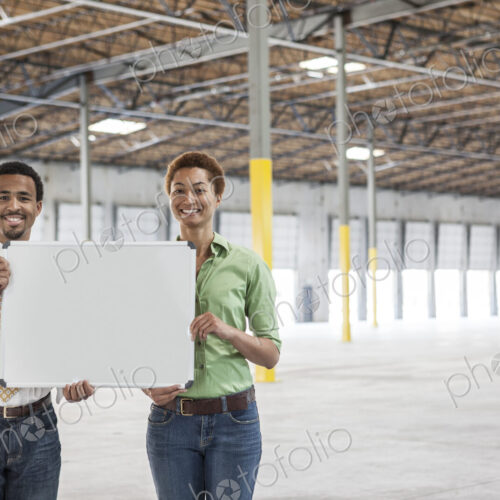 Black man and black woman holding up a blank slate in the interior of a brand new…