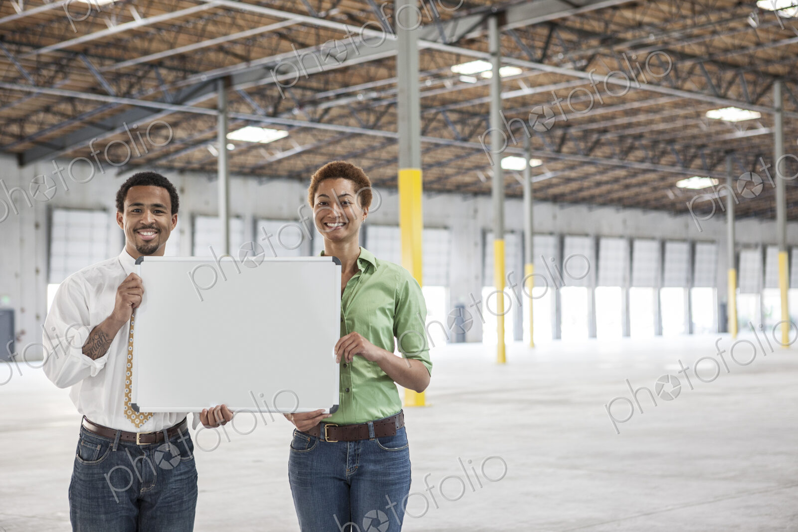 Black man and black woman holding up a blank slate in the interior of a brand new…