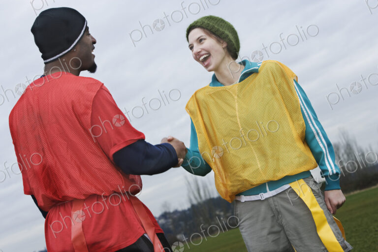 Black man and caucasian woman team members shaking hands at a sporting event.