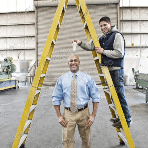 Black man factory owner and young caucasian man factory worker goofing off together on…