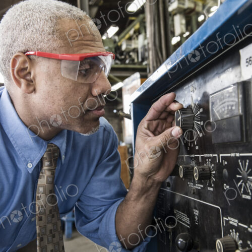 Black man factory owner checking gauges on a piece of welding equipment.