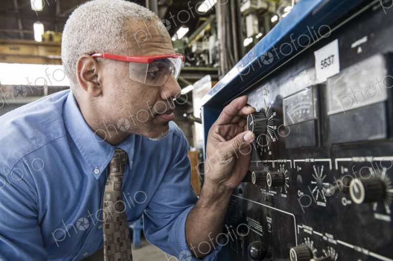 Black man factory owner checking gauges on a piece of welding equipment.