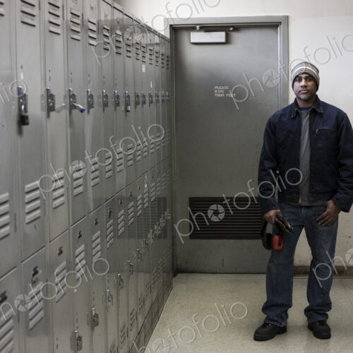 Black man factory worker standing next to lockers in a factory break room.