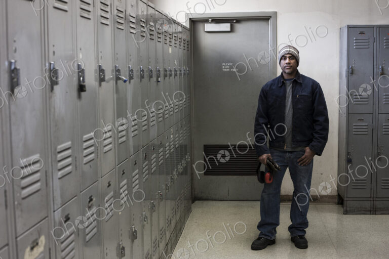 Black man factory worker standing next to lockers in a factory break room.