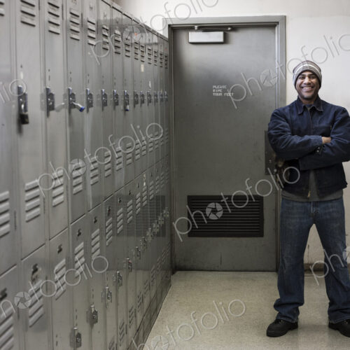 Black man factory worker standing next to lockers in a factory break room.