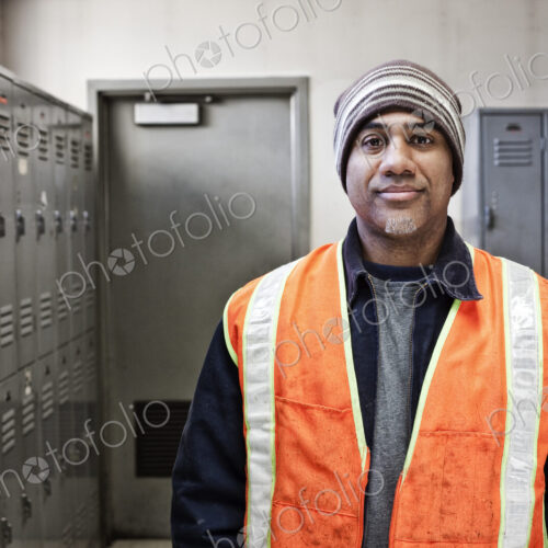 Black man factory worker standing next to lockers in a factory break room.