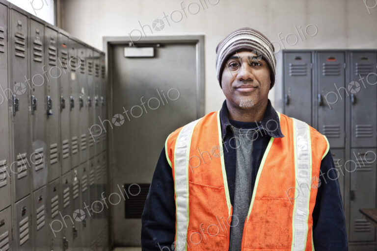 Black man factory worker standing next to lockers in a factory break room.