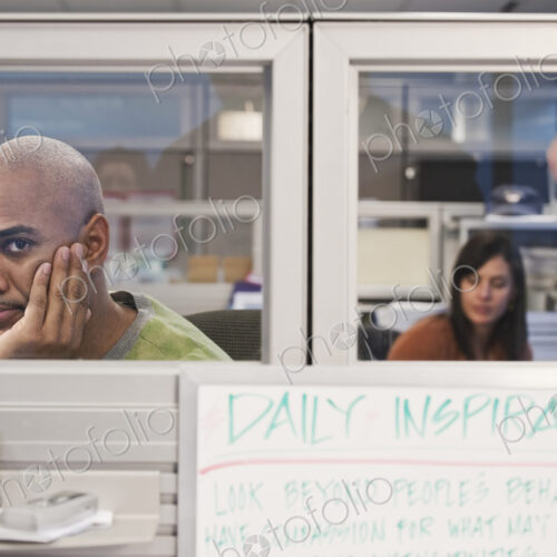 Black man in his office cubicle with co-workers in the background. Black man in his office cubicle with co-workers in the background.