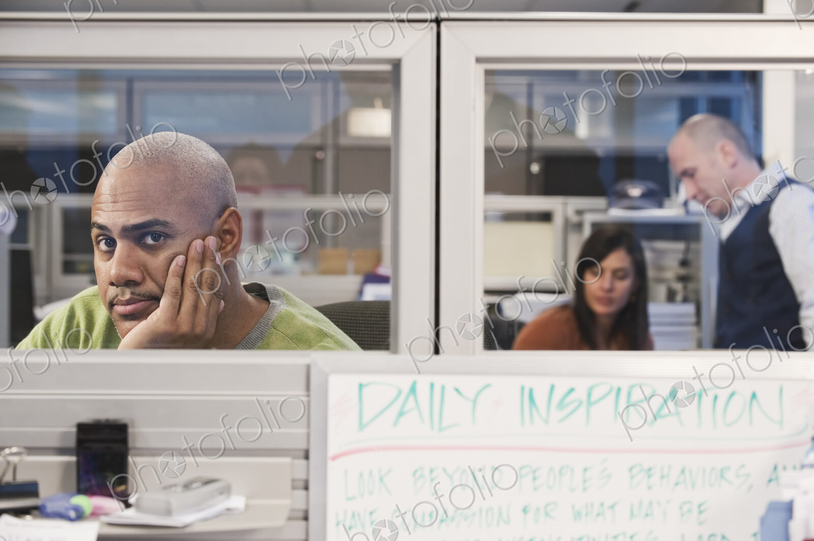Black man in his office cubicle with co-workers in the background.