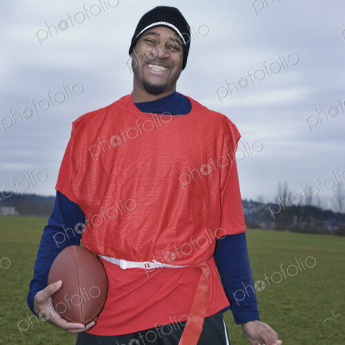 Black man member of an Americn flag football team holding a football and a trophy