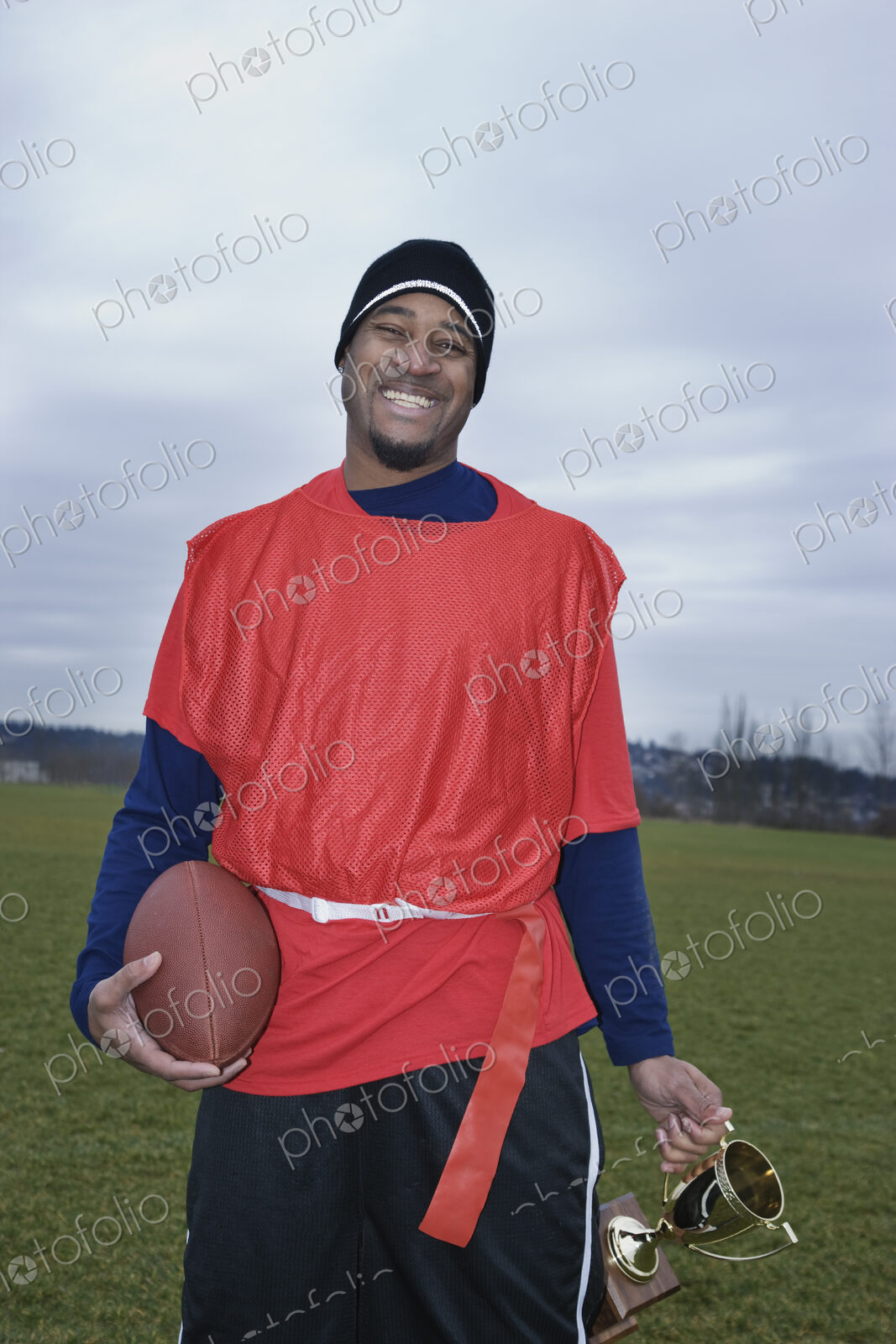 Black man member of an Americn flag football team holding a football and a trophy