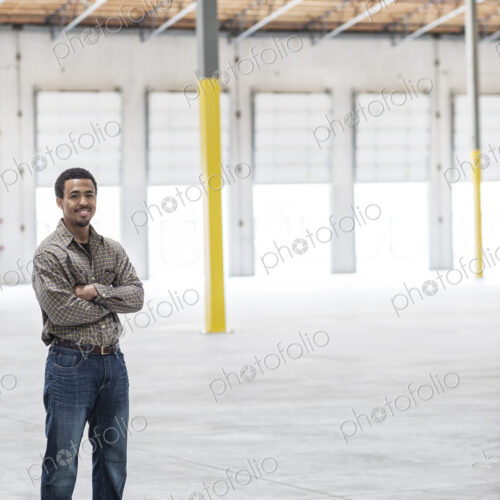 Black man owner of a new warehouse standing inside in front of loading dock doors.