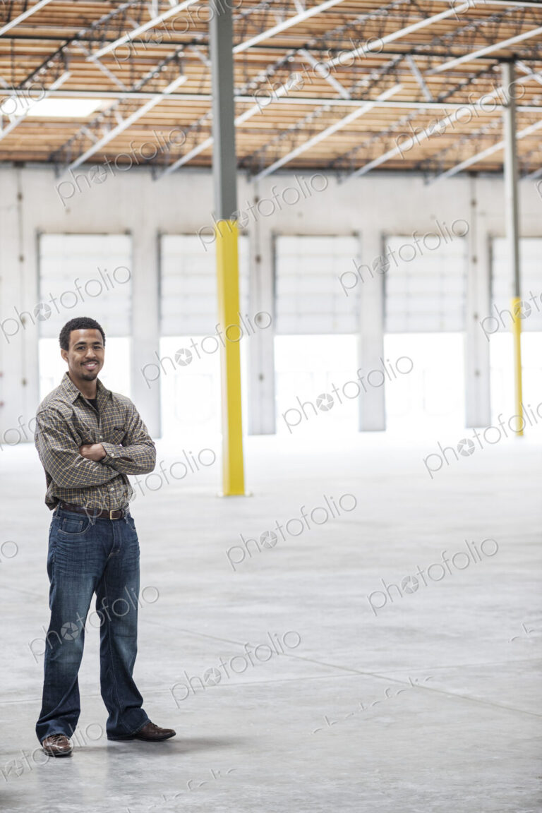 Black man owner of a new warehouse standing inside in front of loading dock doors.
