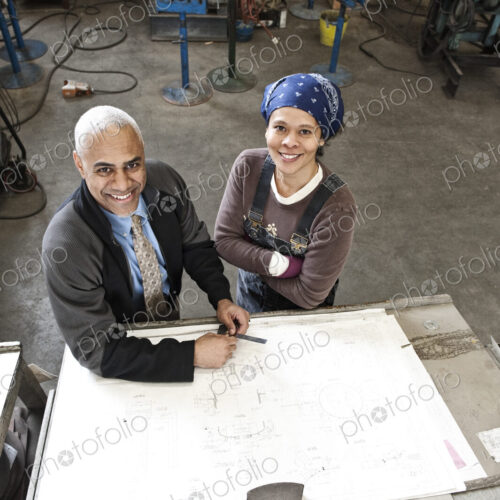 Black man owner of a sheet metal factory and a black woman factory worker goin over…