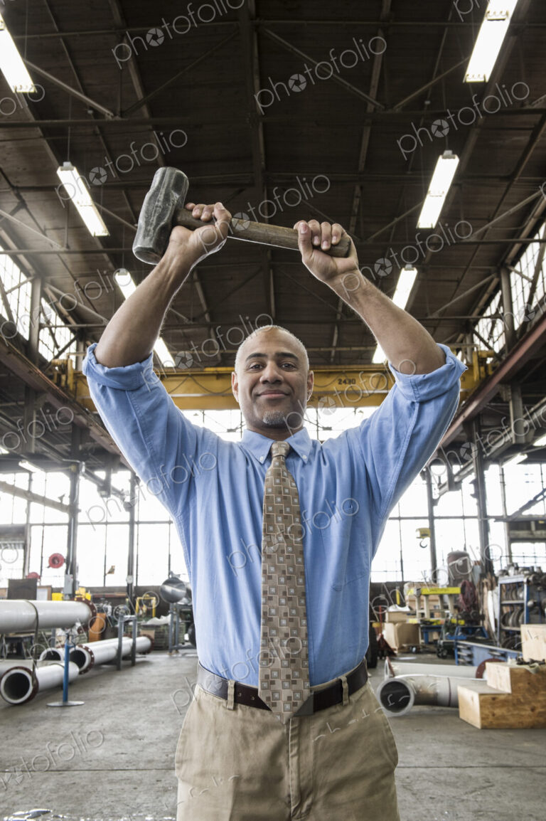Black man owner of a sheet metal factory holding a hammer while standing on the floor…