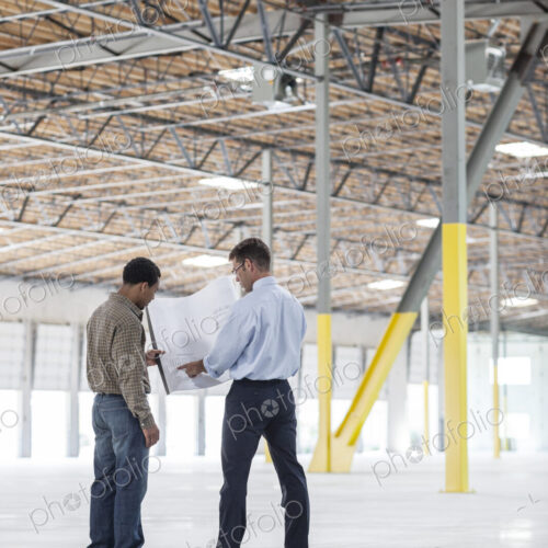 Black man owner of new warehouse and caucasian man architect going over blue print…
