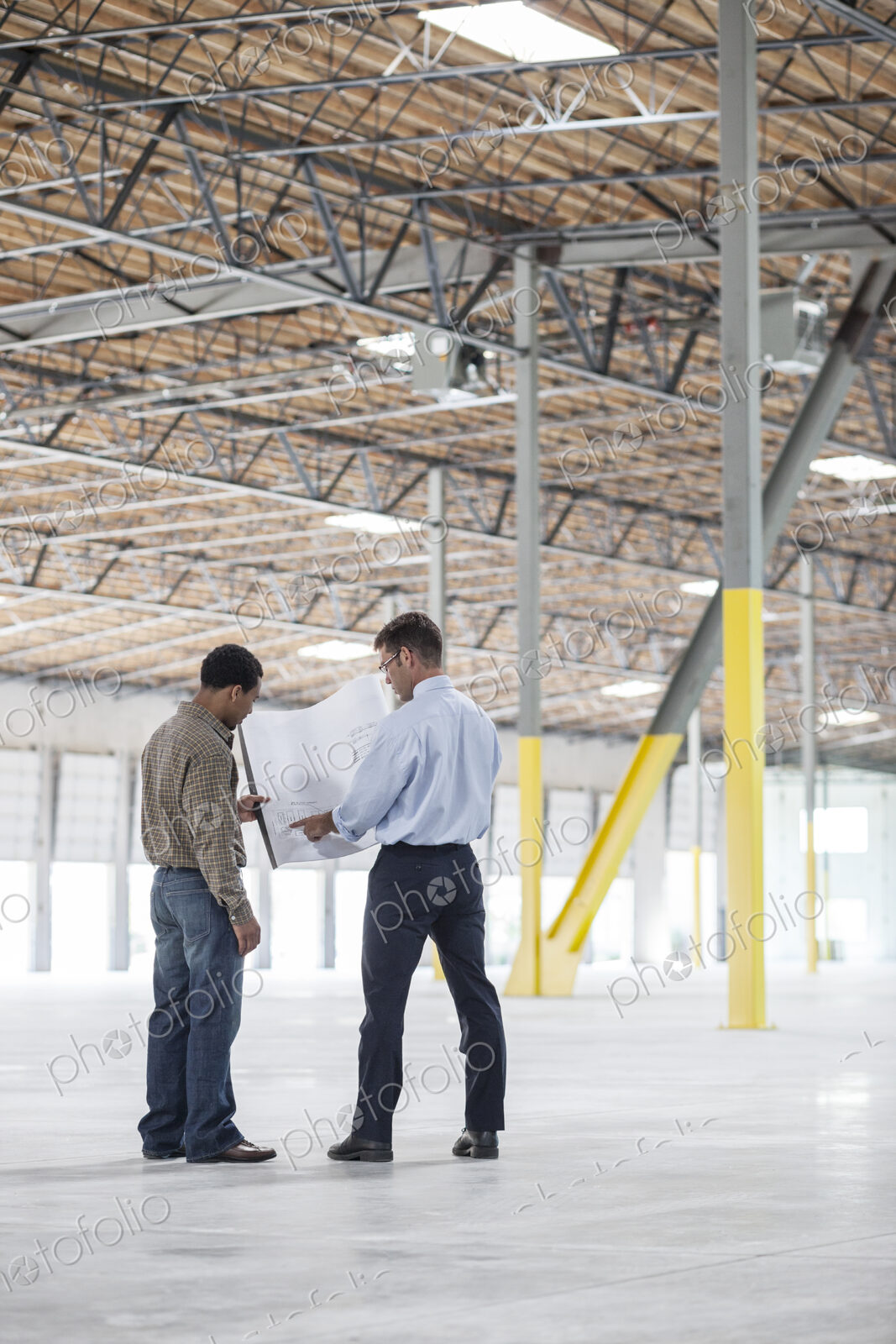 Black man owner of new warehouse and caucasian man architect going over blue print…