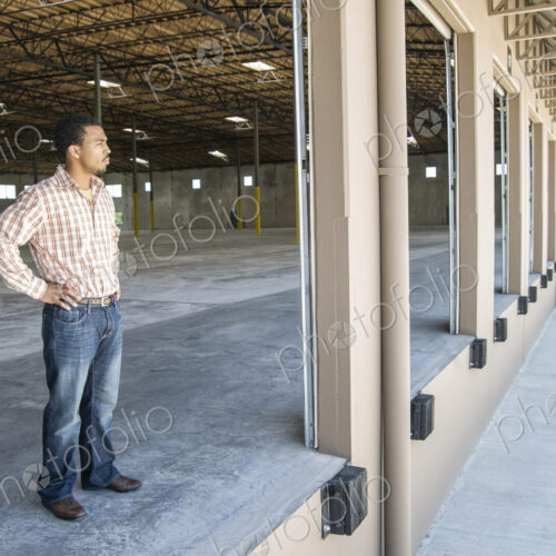 Black man standing in loading dock door of new empty warehouse anticipating the… Black man standing in loading dock door of new empty warehouse anticipating the…
