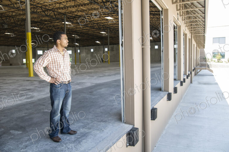 Black man standing in loading dock door of new empty warehouse anticipating the…
