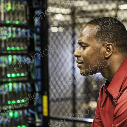 Black man technician doing diagnostic tests on computer servers in server farm.