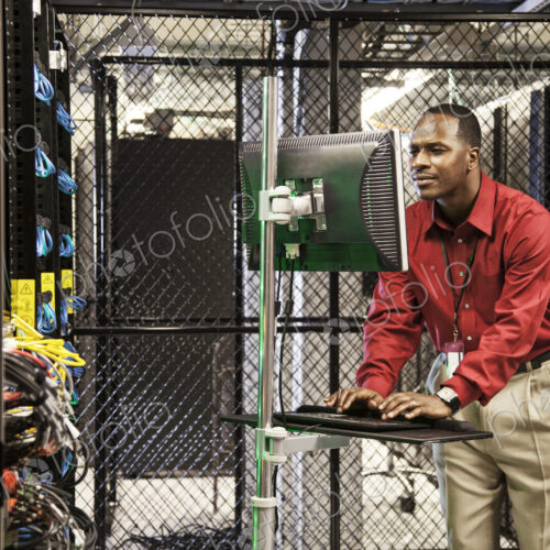 Black man technician doing diagnostic tests on computer servers in server farm. Black man technician doing diagnostic tests on computer servers in server farm.