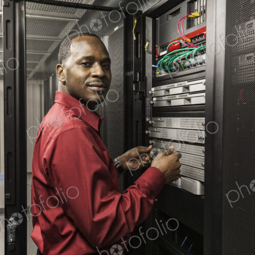 Black man technician working on computer servers in server farm. Black man technician working on computer servers in server farm.