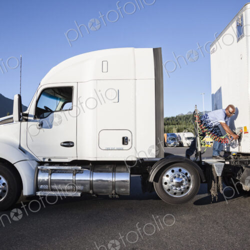 Black man truck driver attaching power cables from truck tractor to trailer at a truck… Black man truck driver attaching power cables from truck tractor to trailer at a truck…