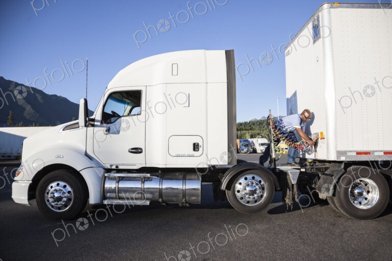 Black man truck driver attaching power cables from truck tractor to trailer at a truck…