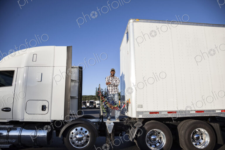 Black man truck driver attaching power cables from truck tractor to trailer at a truck…