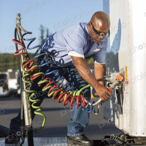 Black man truck driver attaching power cables from truck tractor to trailer at a truck… Black man truck driver attaching power cables from truck tractor to trailer at a truck…