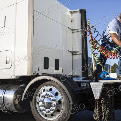 Black man truck driver attaching power cables from truck tractor to trailer at a truck… Black man truck driver attaching power cables from truck tractor to trailer at a truck…