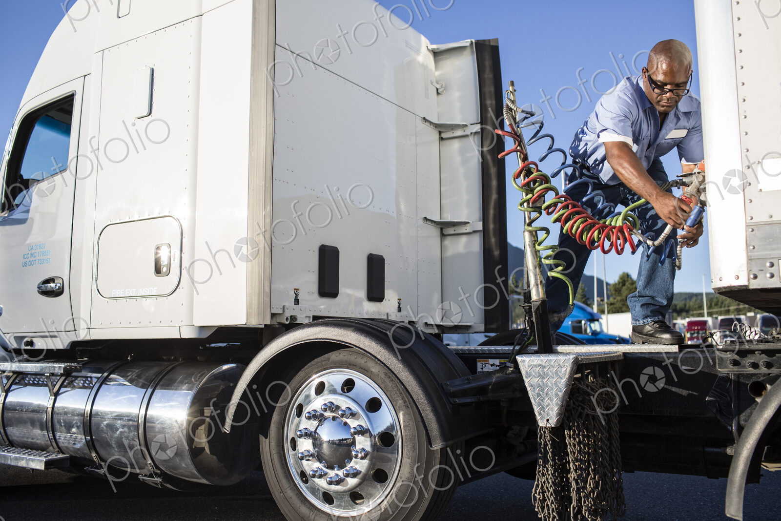 Black man truck driver attaching power cables from truck tractor to trailer at a truck…