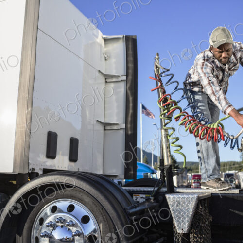 Black man truck driver attaching power cables from truck tractor to trailer at a truck… Black man truck driver attaching power cables from truck tractor to trailer at a truck…