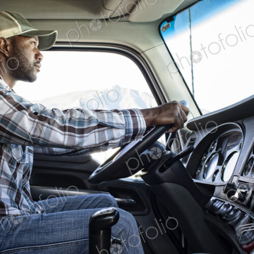 Black man truck driver in the cab of his commercial truck.